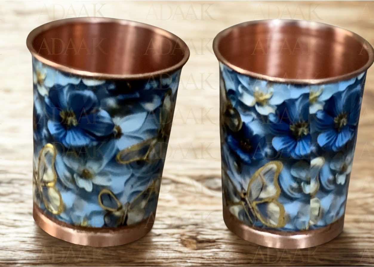 Two copper cups with blue floral design on a wooden surface