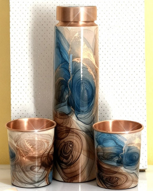 Copper tumblers with marbled design on a white surface against a yellow wall, featuring ADAAK branding.