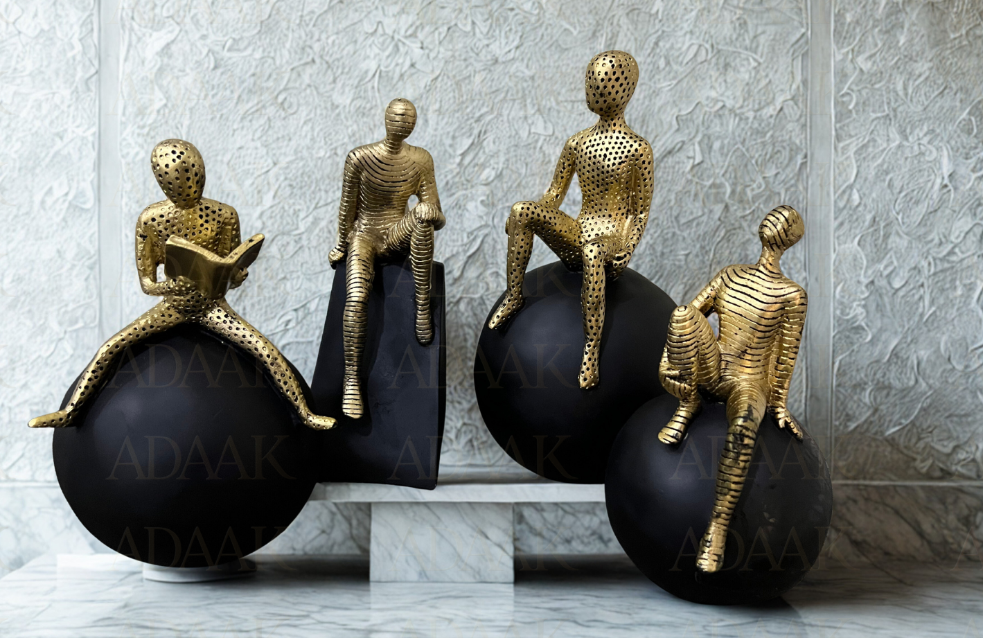 Decorative sculptures of gold figures on black spheres against a textured wall.