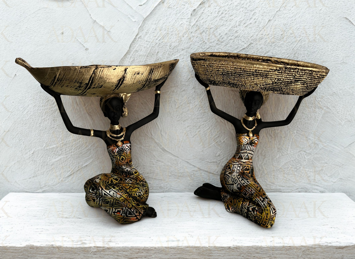 Two decorative bowls on stands with black figures holding them against a light gray background.