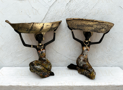 Two decorative bowls on stands with black figures holding them against a light gray background.